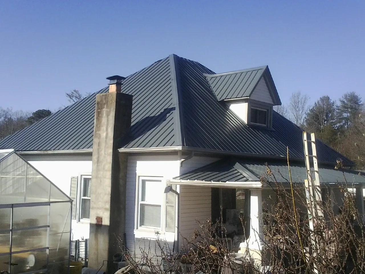 Dark blue standing seam metal roof on a white farmhouse with dormer — Slate & Tile Roof Repair by Roofing Brothers in Phil Campbell