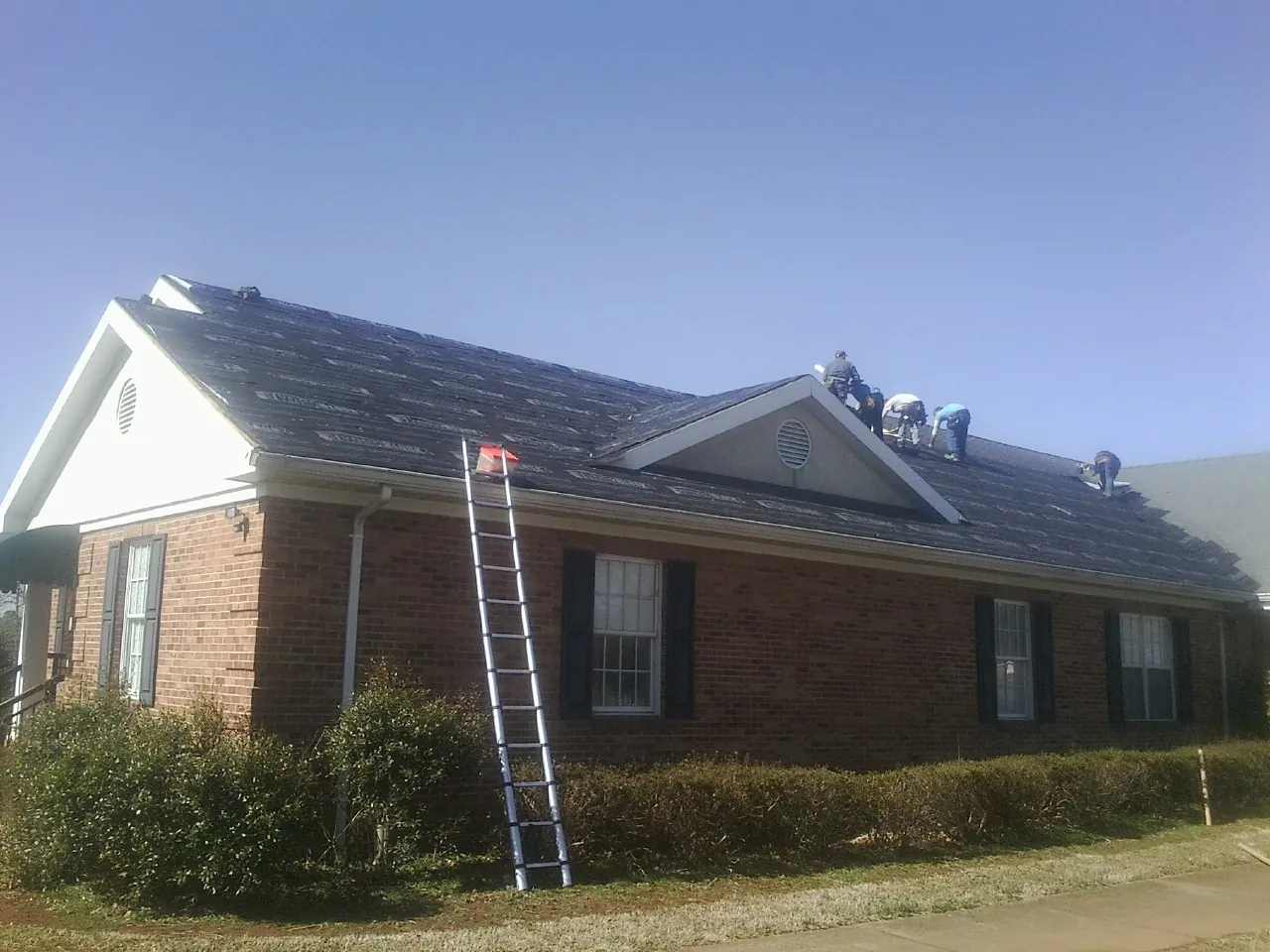 Crew tearing shingles off a brick ranch roof with a ladder set — Emergency Roof Repair work by our crew in Phil Campbell