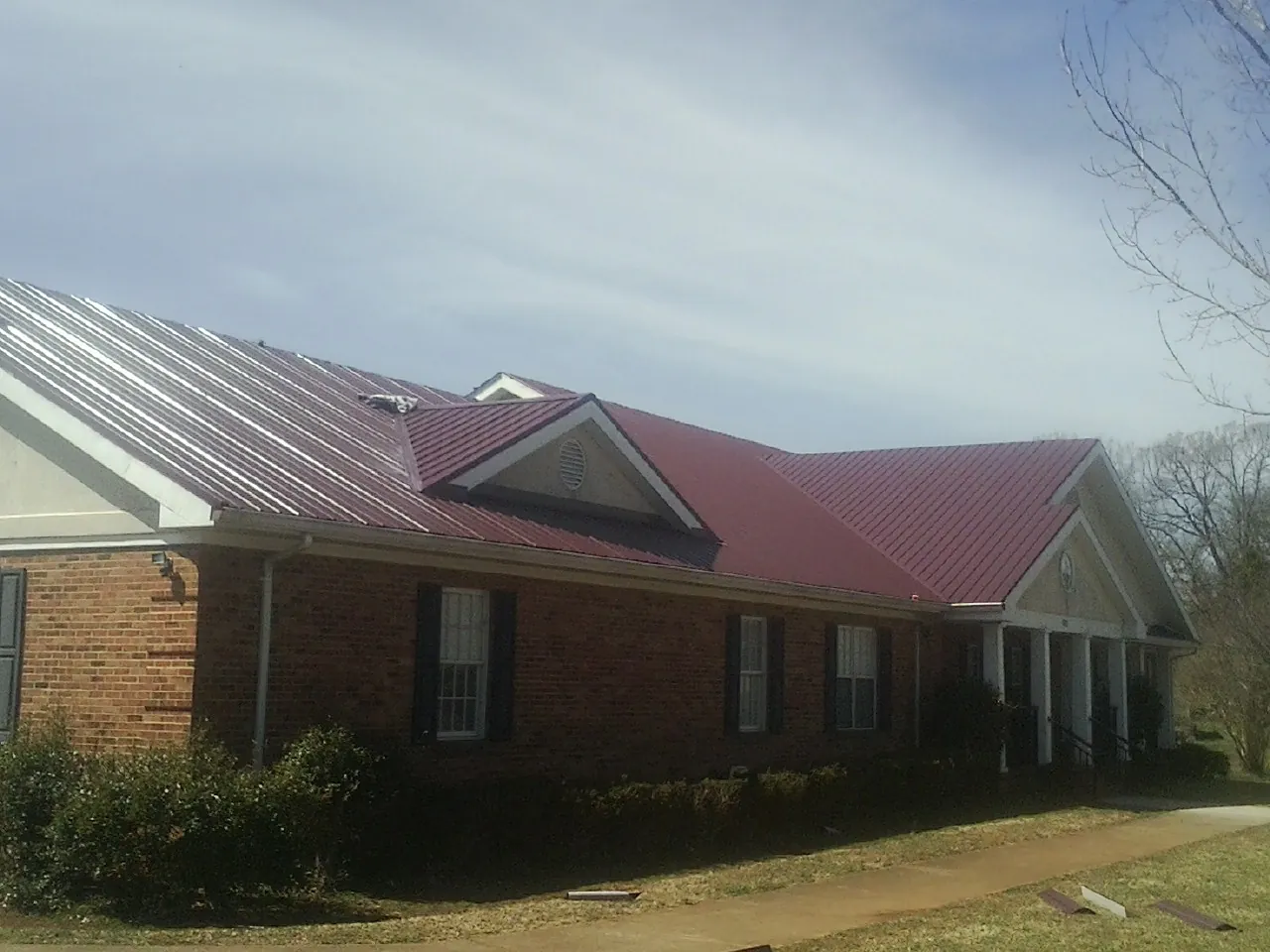 Red metal roof with gabled entries on a long brick building, from a Hail Damage Roof Repair job in Phil Campbell