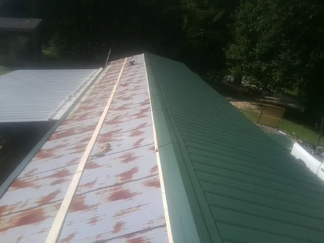 Old rusted panels beside newly installed green metal roofing — Wind Damage Roof Repair by Roofing Brothers in Phil Campbell