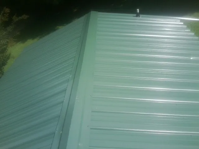 New green metal panels meeting at the ridge of a roof — Flat Roof Repair work by our crew in Phil Campbell