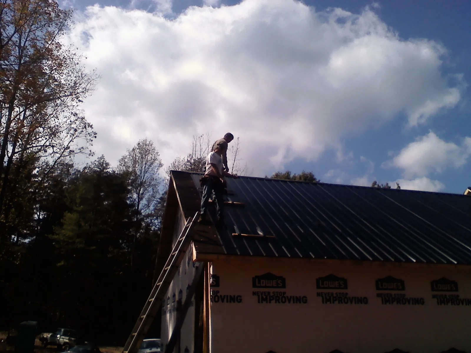 Roofer fastening dark metal panels high against a cloudy sky, from a Roof Inspection job in Phil Campbell