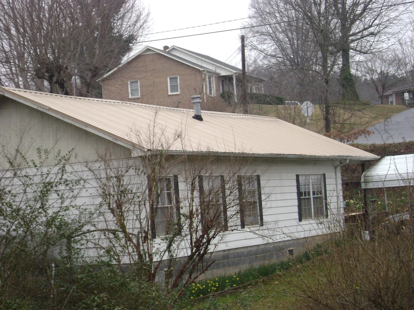Tan metal roof on a white sided house set into a hillside — Commercial Roofing by Roofing Brothers in Phil Campbell