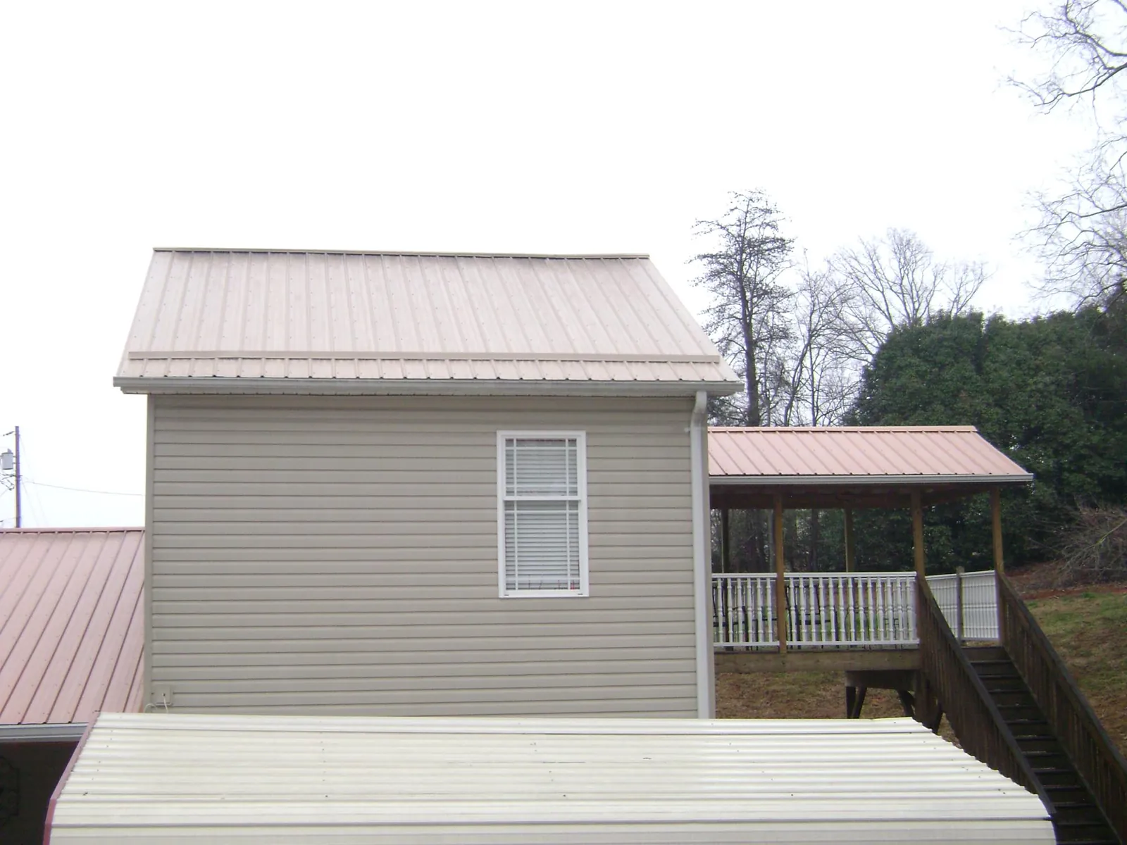 Tan metal roofs on a two story addition and attached porch, from a Roof Replacement job in Phil Campbell
